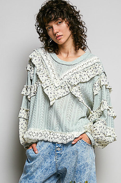 Person wearing a light blue embroidered pants and a matching top with ruffled details on a plain background
