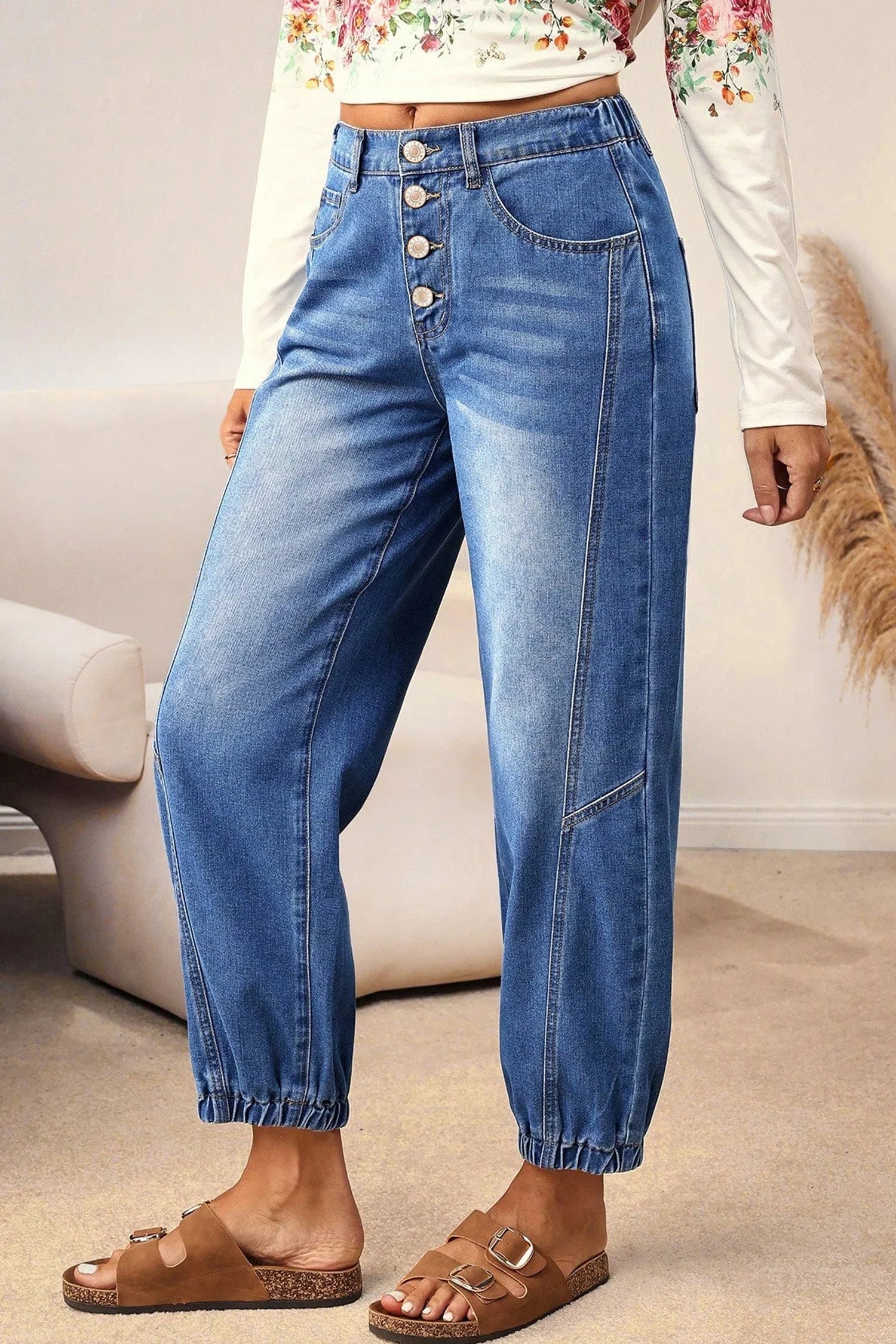 Person wearing blue jeans with a white top and brown sandals in a room setting.