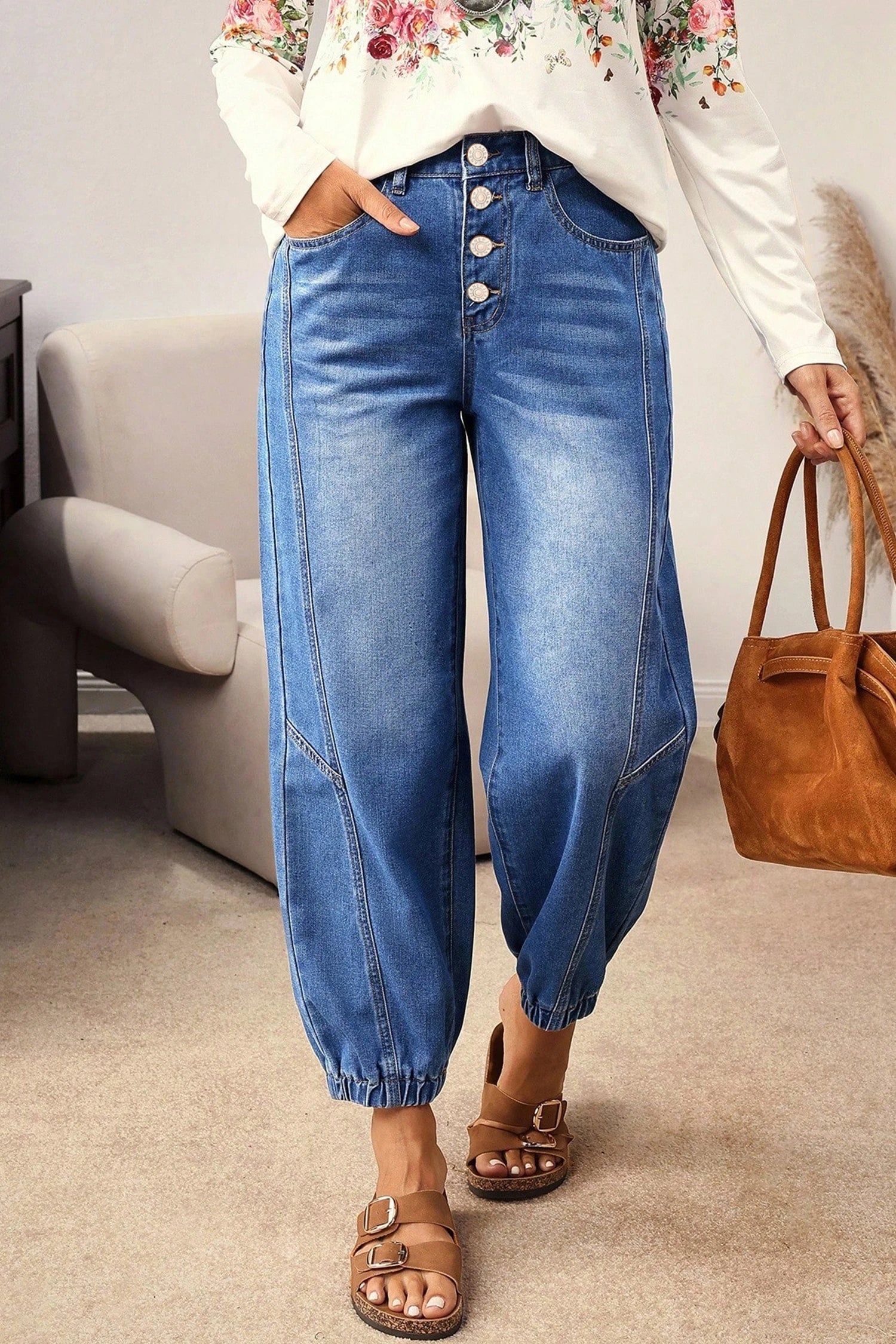 Person wearing blue jeans and a floral top, holding a brown handbag indoors.