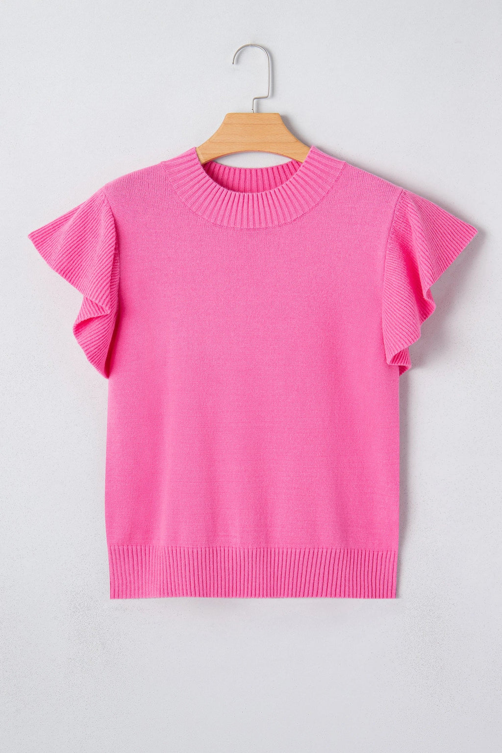 Pink sweater with ruffled sleeves on a hanger against a light gray background