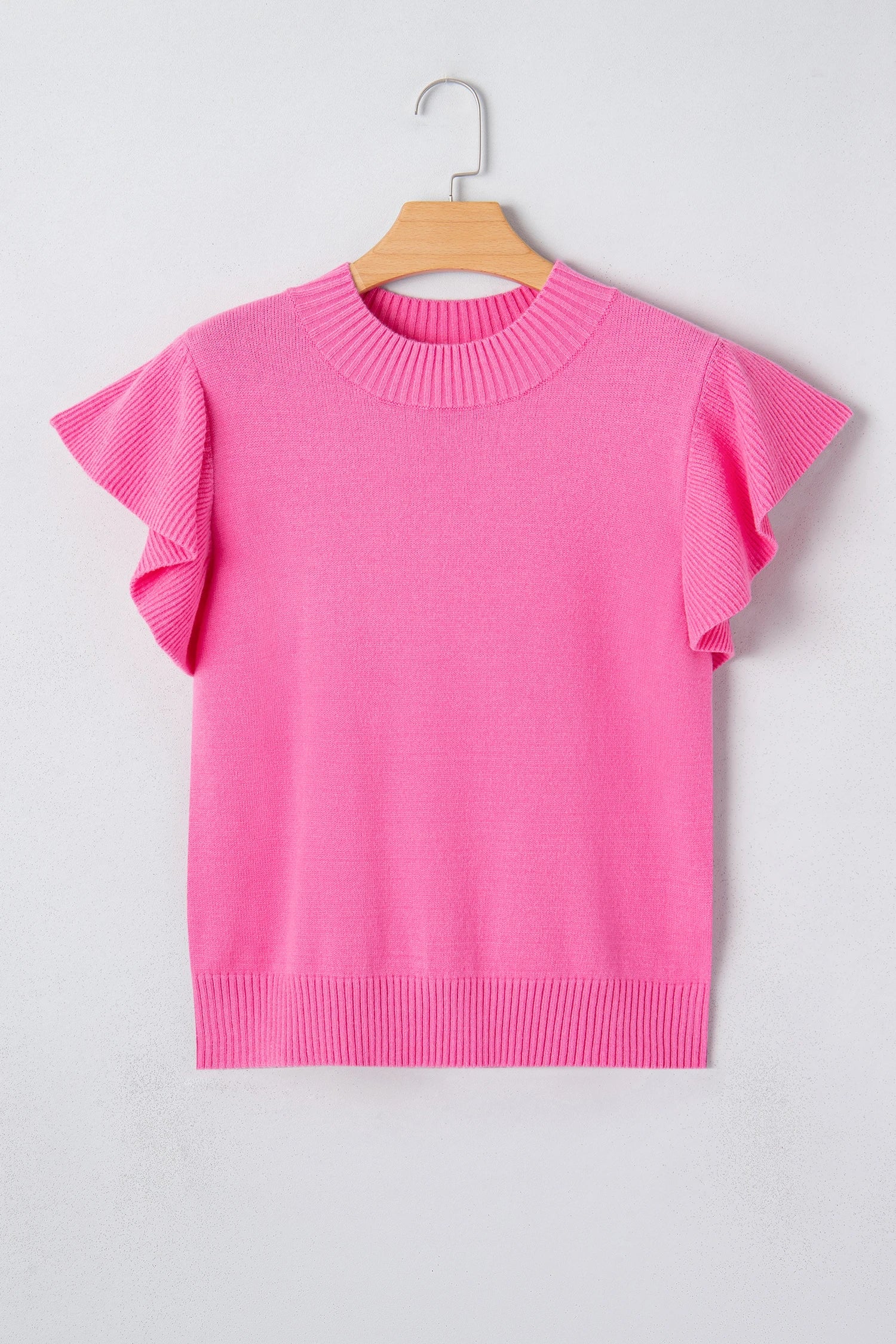 Pink sweater with ruffled sleeves on a hanger against a light gray background