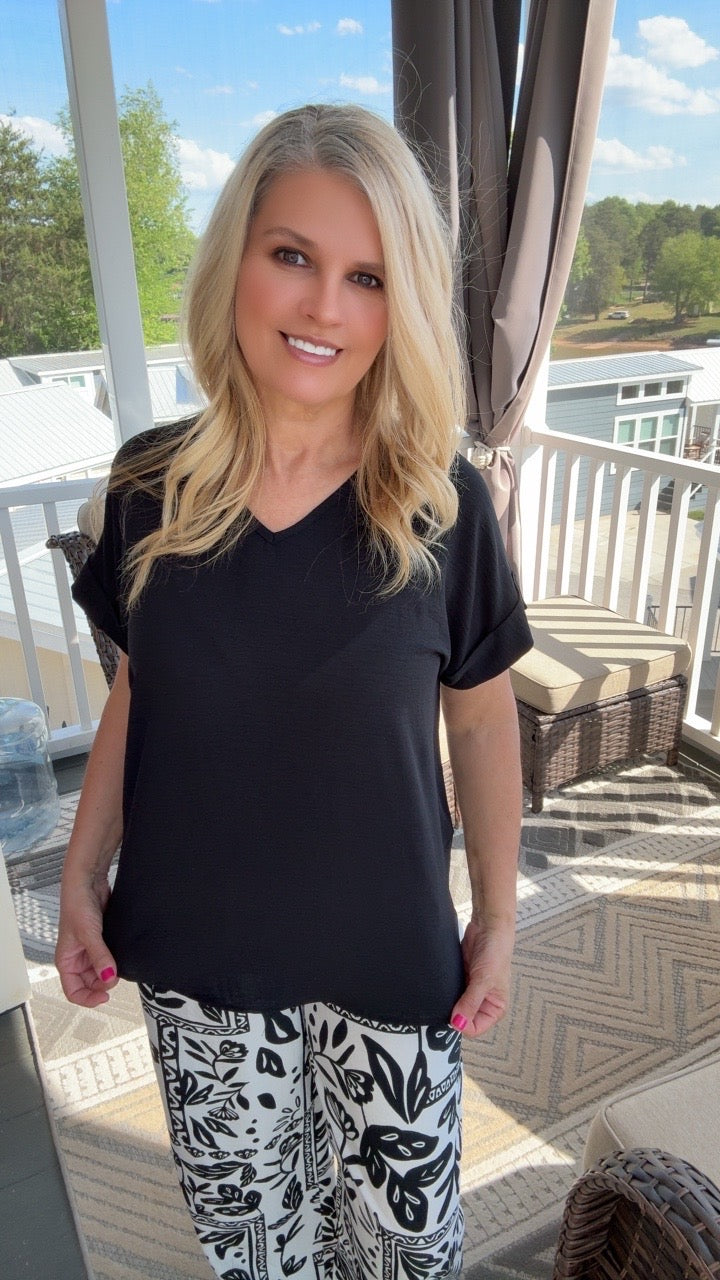 Woman wearing a black top and patterned pants standing on a patio.