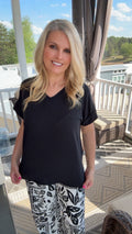 Woman wearing a black top and patterned pants standing on a patio.