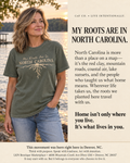 A woman wearing an olive green graphic t-shirt with 'My Roots Are In North Carolina' printed on the front, standing outdoors near a body of water. The image is split into two columns: the left shows the model wearing the shirt, and the right features a beige text block with promotional copy for LKN Boutique.